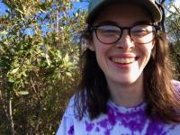 Image of UC Davis student Caitlin Brown outdoors, in front of green leafy bushes.