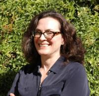 head and shoulders of woman with dark hair, dark framed glasses, dark blouse in front of plants