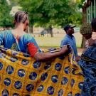 Women, one holding a colorful wrap, and another carrying a baby on her back, line up at a health clinic in Tanzania.