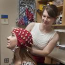 Photo of researcher adjusting an EEG cap on a young woman.