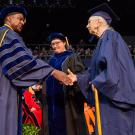 Photo of elderly woman in UC Davis graduation robes shaking hands with chancellor on commencement stage