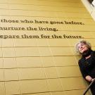 Photo: historian under sign, "Remember those who have gone before, nurture the living and prepare them for the future."