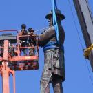 workers in a cherry picker next to statue