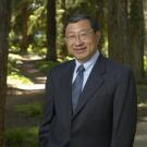 Photo of UC Davis physicist and former dean Winston Ko, wearing a suit, standing in a UC Davis redwood grove.