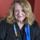 Woman with blond hair head tilted downward, wearing black blouse and blue scarf 