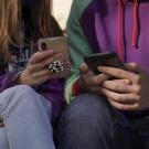 Two students look at their cell phones in a close up photo