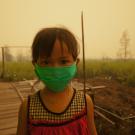 Young girl wearing face mask outdoors, smoke haze fills sky behind her
