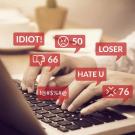 Hands on a laptop keyboard with red thought bubbles with words "Idiot!" "Hate U" and "Loser," icons for "Don't Like" and symbols representing expletives.