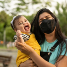 Joyful baby with masked mom in a park