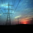 Electric power transmission lines with sun on horizon, glowing pink against a dark blue sky.
