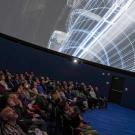 About 100 people sitting in a theater looking upwards at a planeterium screen.