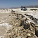 A fault scarp from the Ridgecrest earthquake cuts across a dry lake bed with a white truck in the background.