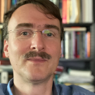 UC Davis economist, wearing glasses and mustache, bookshelves behind nim