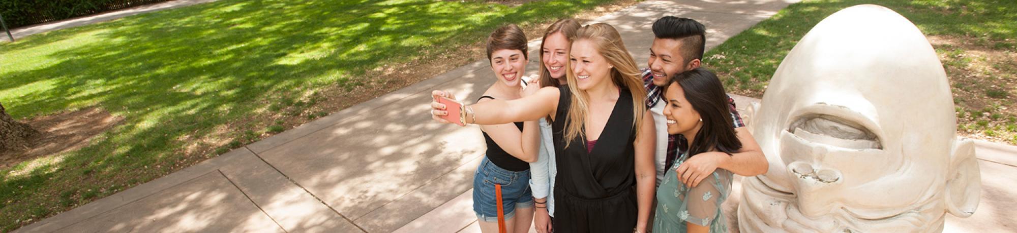 Students take a selfie in front of an Egghead statue