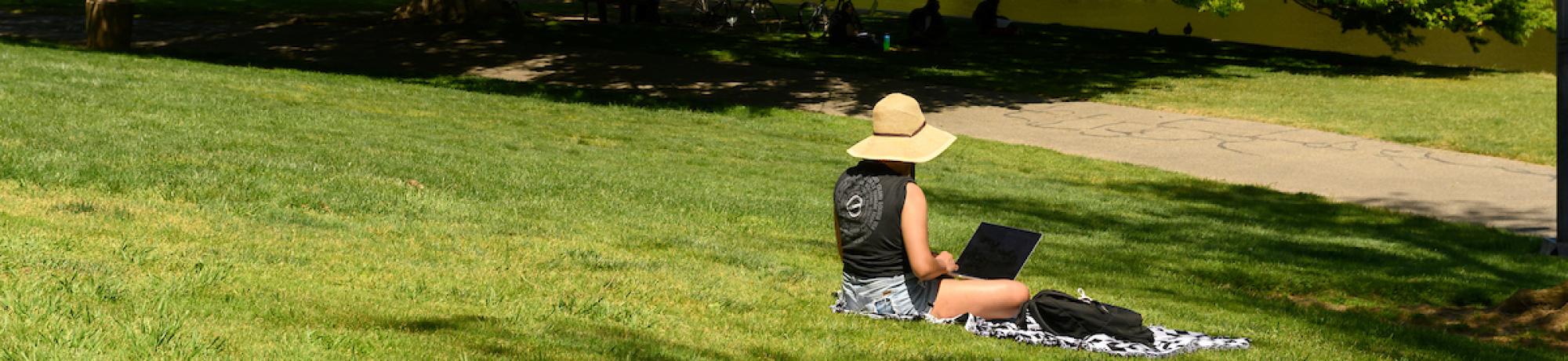 student sitting on grass with laptop