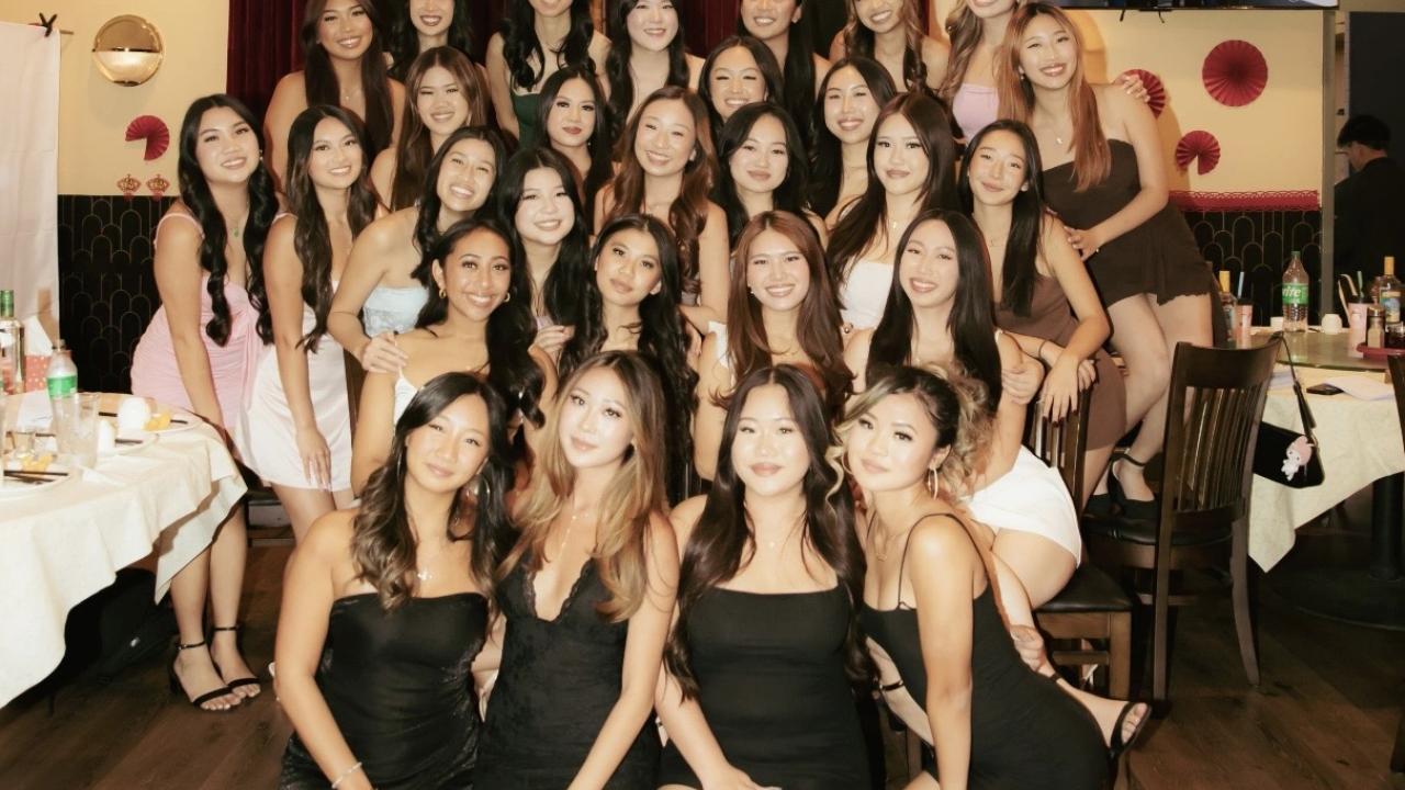 Smiling group of women in black dresses posing in a decorated banquet hall