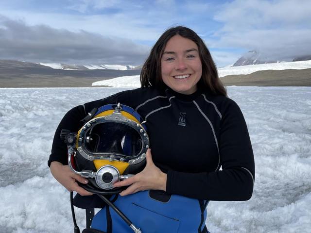 Woman wearing a diving suit and holding a diving helmet standing among a snowy landscape