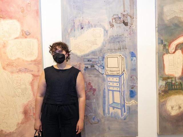 Artist standing between their hung work which is orange and blue