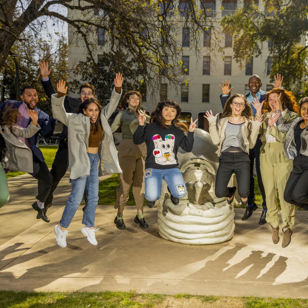 A group of students leap into the air in front of an Egghead sculpture