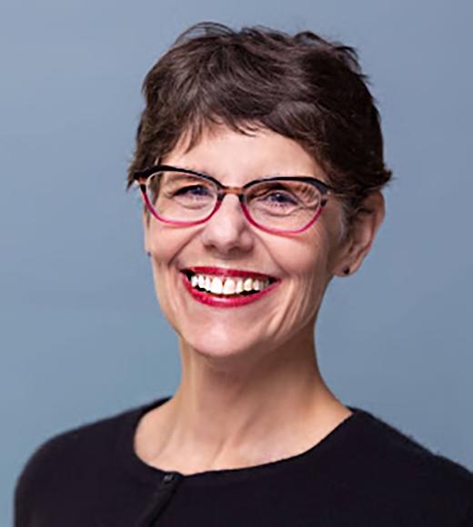 Headshot of mature smiling woman with very short dark brown hair, red eyeglasses, black cardigan sweater
