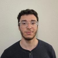 Headshot photograph — young man with clear glasses, curly dark hair, slight smile