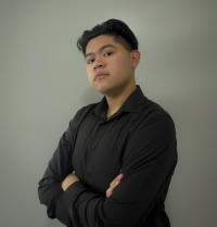 Young man headshot, arms crossed, black shirt, neutral gray background, confident expression
