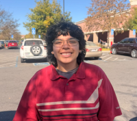 Smiling person with curly hair and glasses wearing red striped shirt in parking lot (photo)
