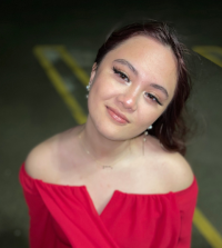 Smiling Asian American female student with dark brown hair and long eyelashes, wearing an off-shoulder bright red top