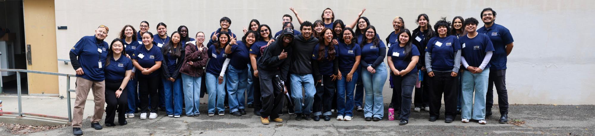 Large team in navy shirts standing outdoors against a beige wall, smiling